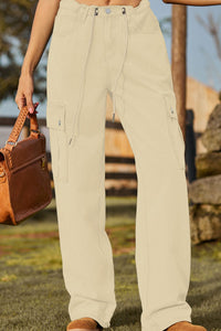 Person wearing beige cargo pants holding a brown leather bag outdoors.
