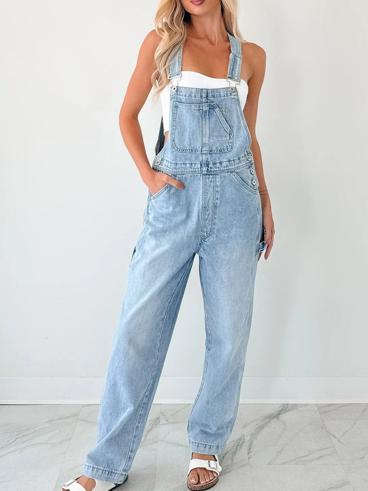 Person wearing light blue denim overalls on a white background