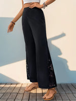 Person wearing black wide-leg pants with floral details against a light blue wall.