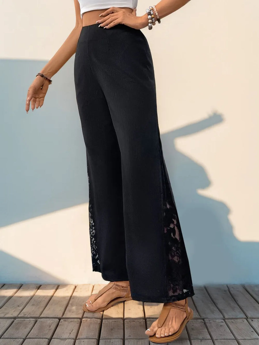 Person wearing black wide-leg pants with floral details against a light blue wall.