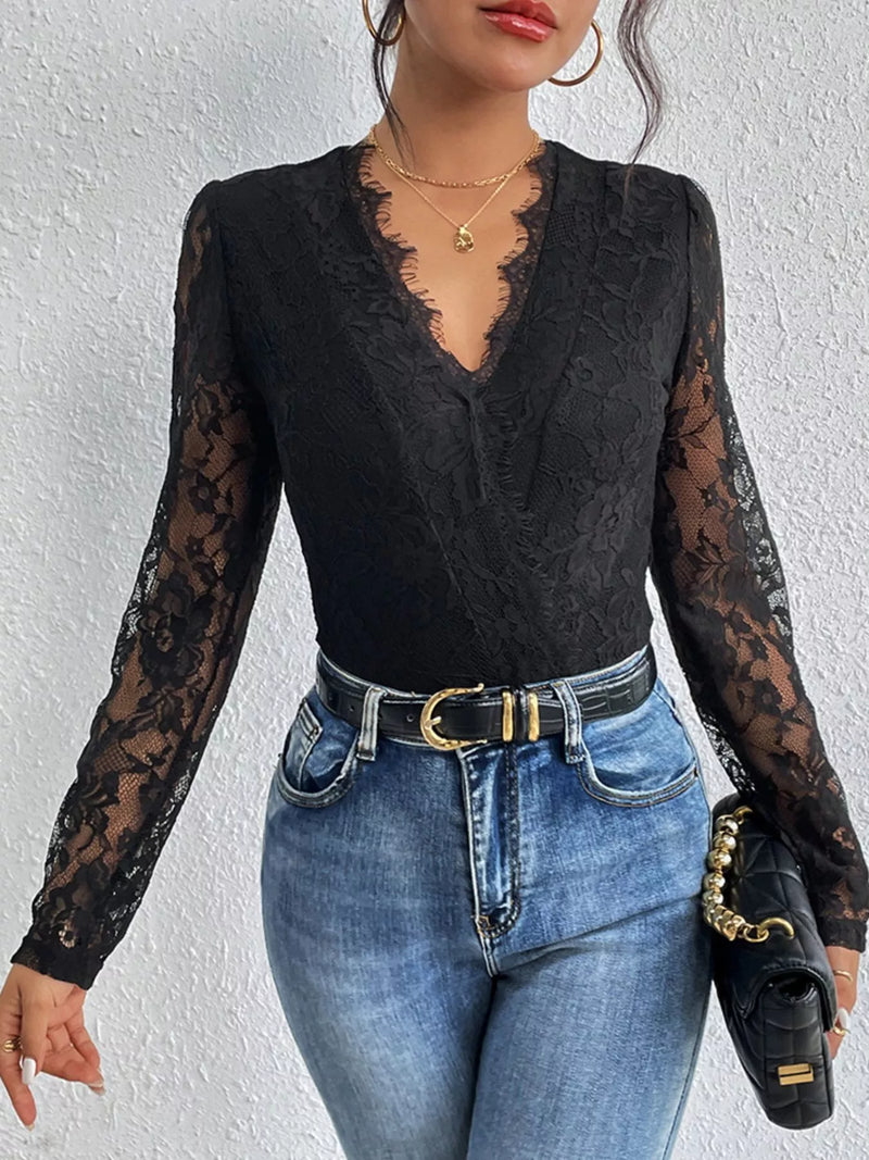 Person wearing a black lace long-sleeve top and blue jeans against a white background
