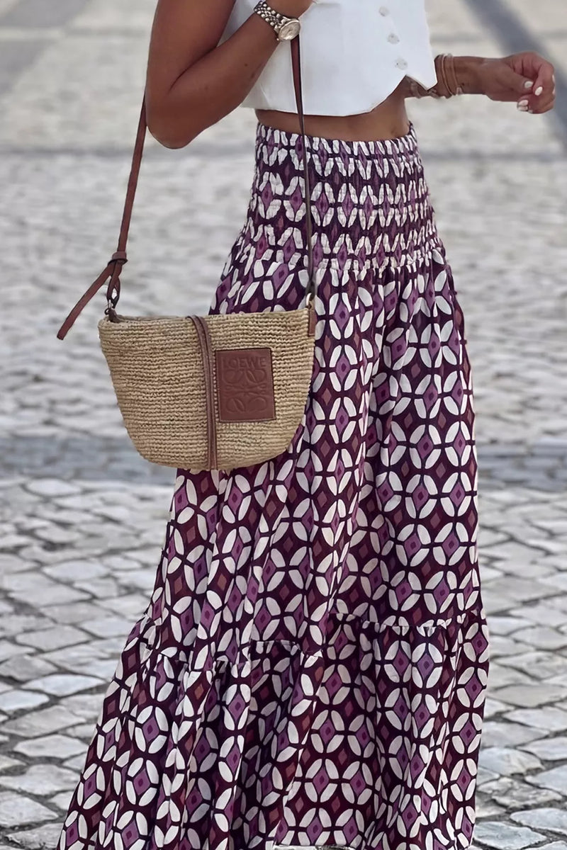 Person wearing a patterned skirt and holding a straw bag on a cobblestone street.