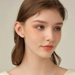Close-up of a woman wearing a delicate earring against a neutral background