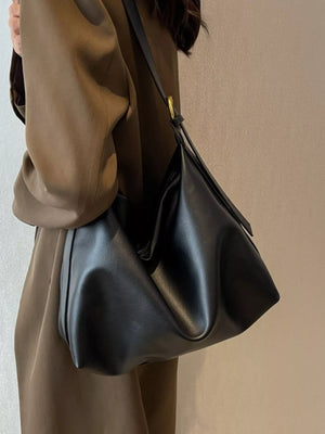 Person wearing a brown coat holding a black handbag against a neutral background