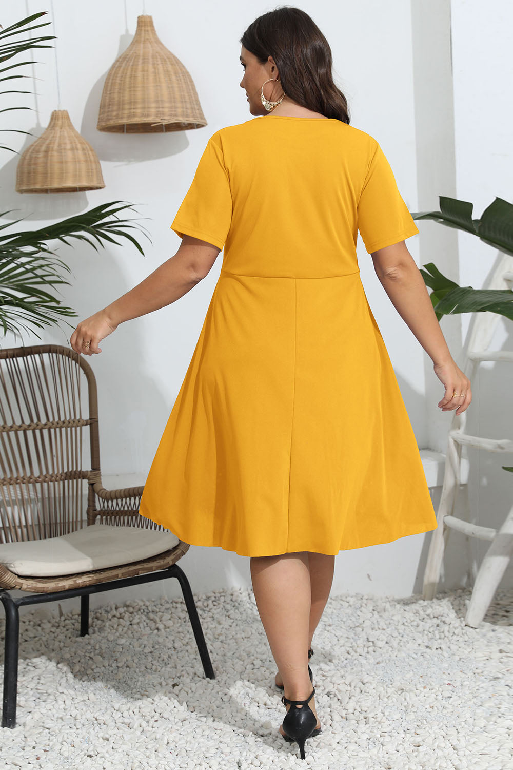 Woman wearing a yellow dress in an indoor setting with plants and a chair.