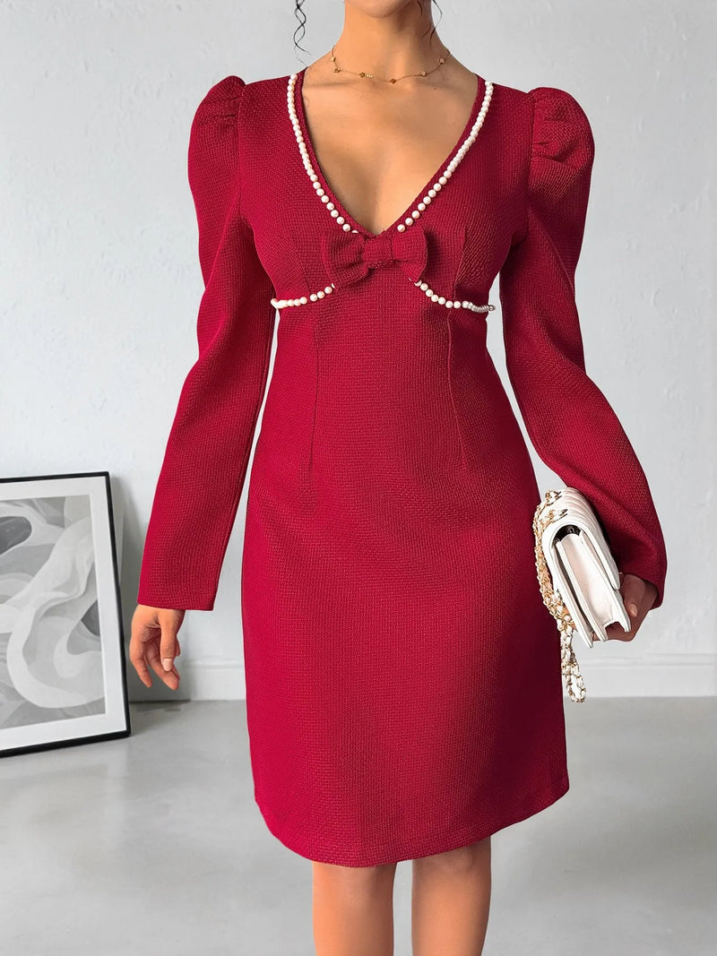 Red dress with pearl details worn by a person, standing against a plain background.
