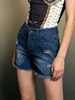 Person wearing blue denim shorts with a patterned top on a neutral background