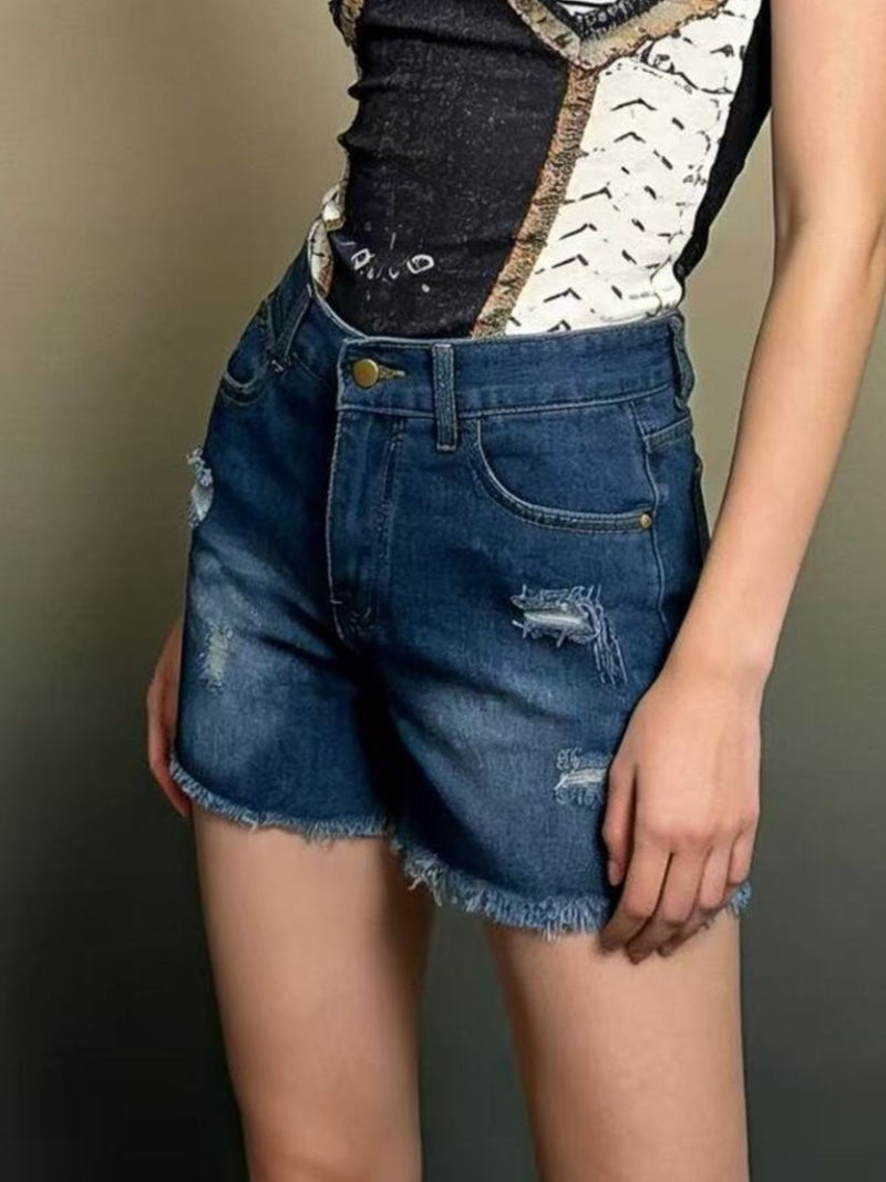 Person wearing blue denim shorts with a patterned top on a neutral background