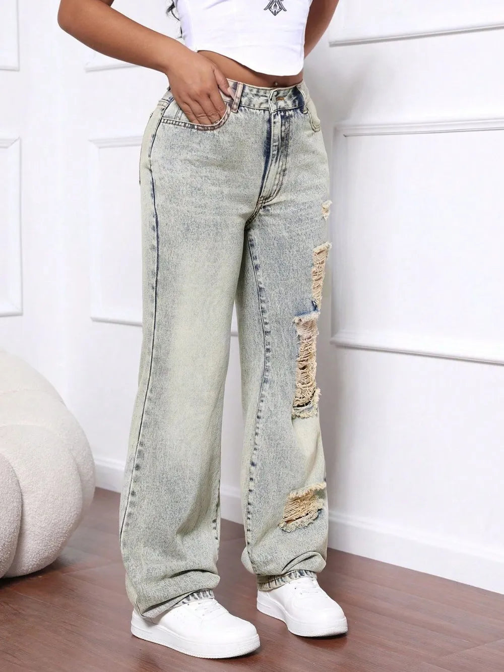 Person wearing light blue distressed jeans and white sneakers on a wooden floor.
