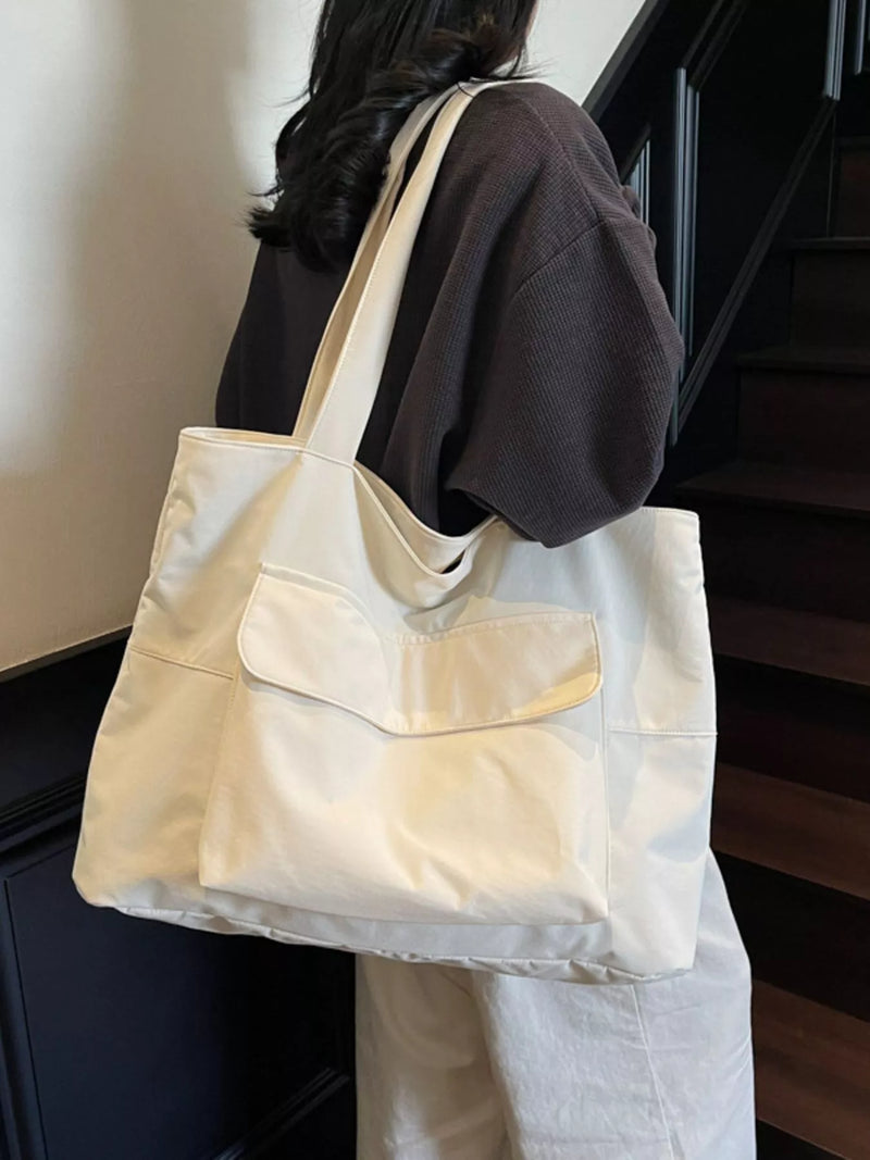Person carrying a beige tote bag with a pocket, standing indoors.
