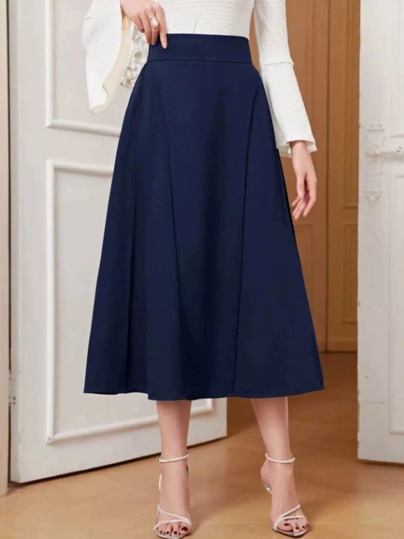 Person wearing a navy blue skirt with a white top in a minimal indoor setting