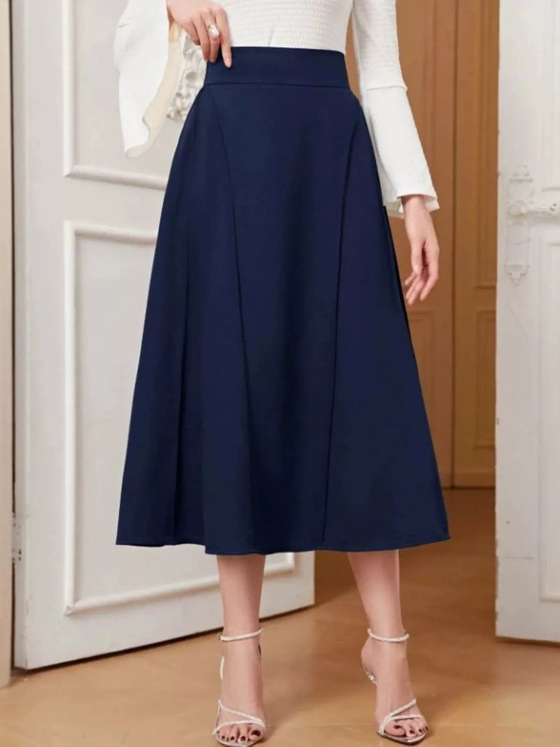 Person wearing a navy blue skirt with a white top in a minimal indoor setting
