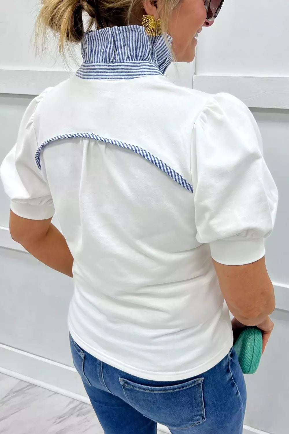 Person wearing a white shirt with blue trim and blue jeans, standing against a white background.