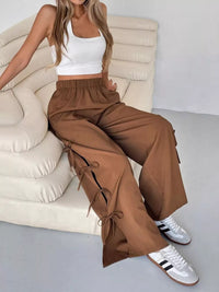 Person wearing a white crop top and brown wide-leg pants sitting on a beige couch.