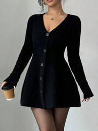 Person wearing a black cardigan over a black dress, holding a coffee cup.