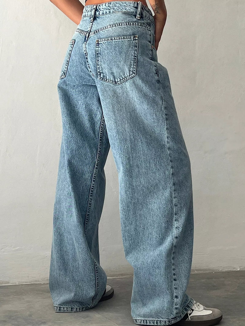 A person wearing light-wash blue wide-leg denim jeans, shown from the back against a plain light gray wall and concrete floor.