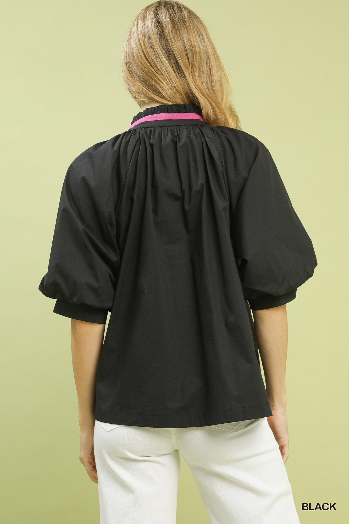 Person wearing a black blouse with a pink collar against a light green background