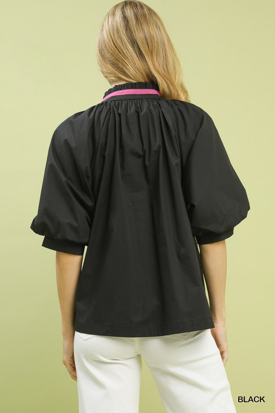 Person wearing a black blouse with a pink collar against a light green background