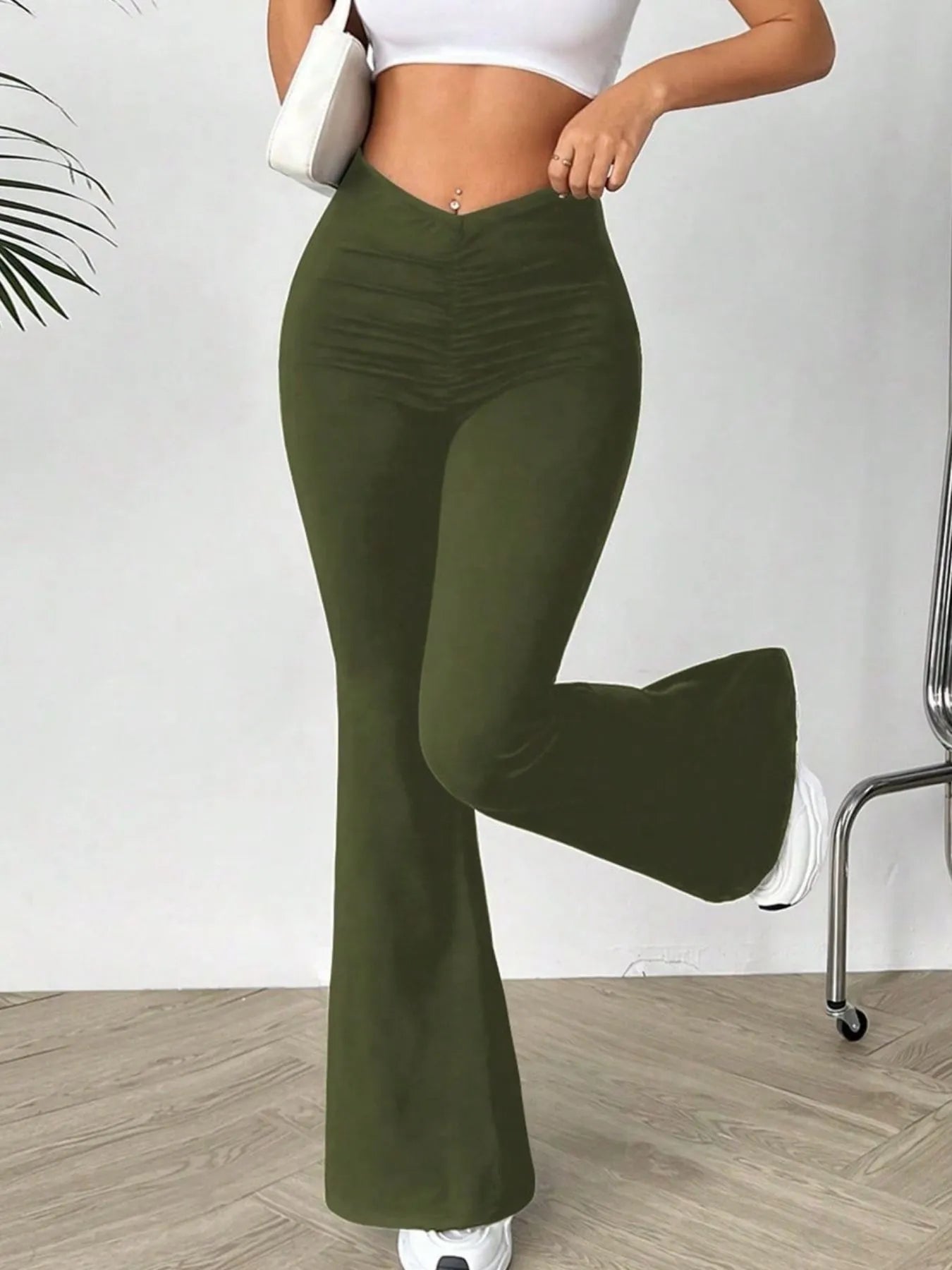 Person wearing olive green flared pants with a white top and shoes on a plain background