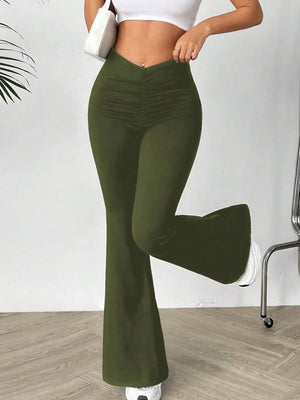 Person wearing olive green flared pants with a white top and shoes on a plain background