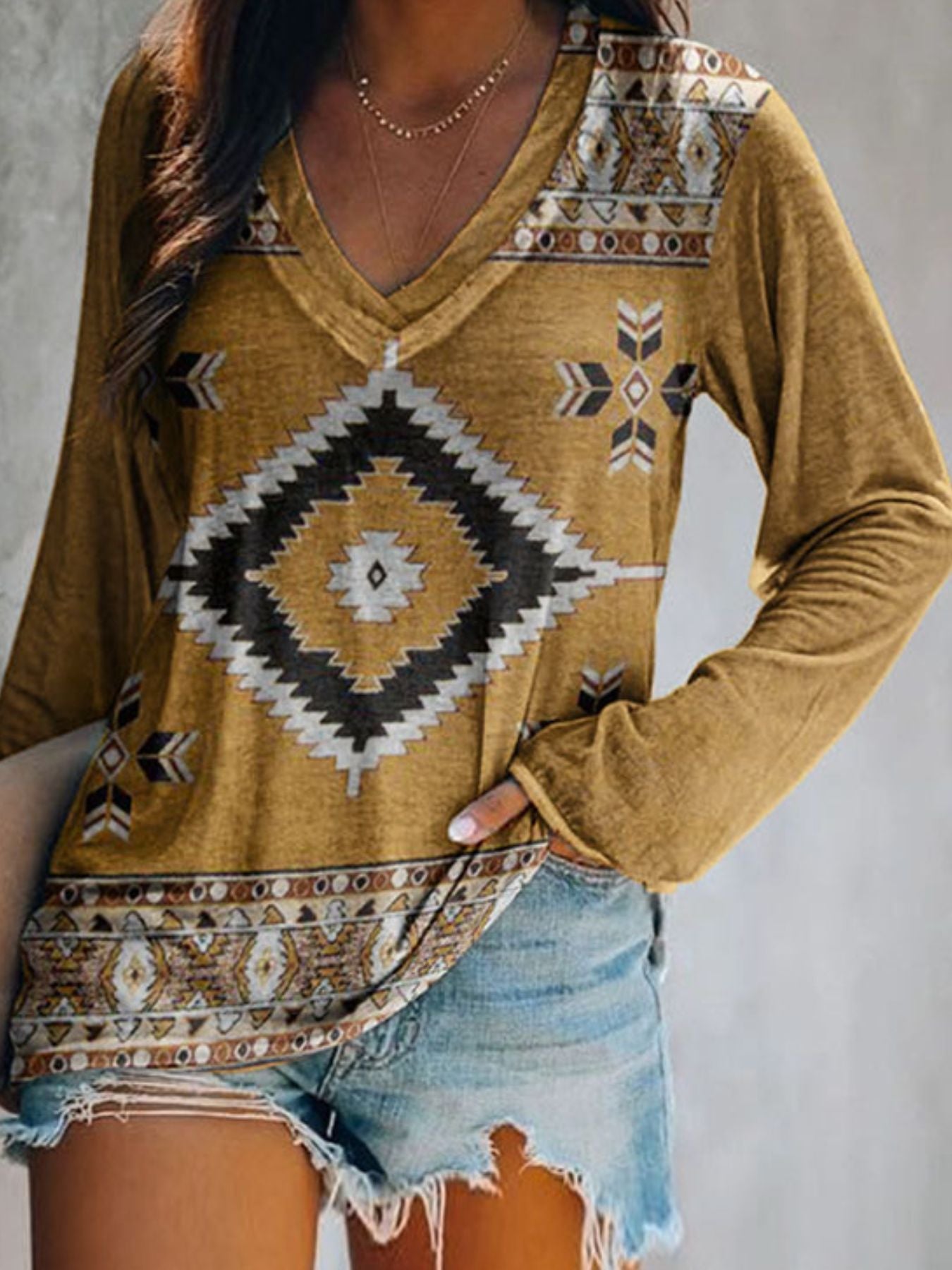 Person wearing a mustard yellow long-sleeve top with tribal pattern and denim shorts on a plain background