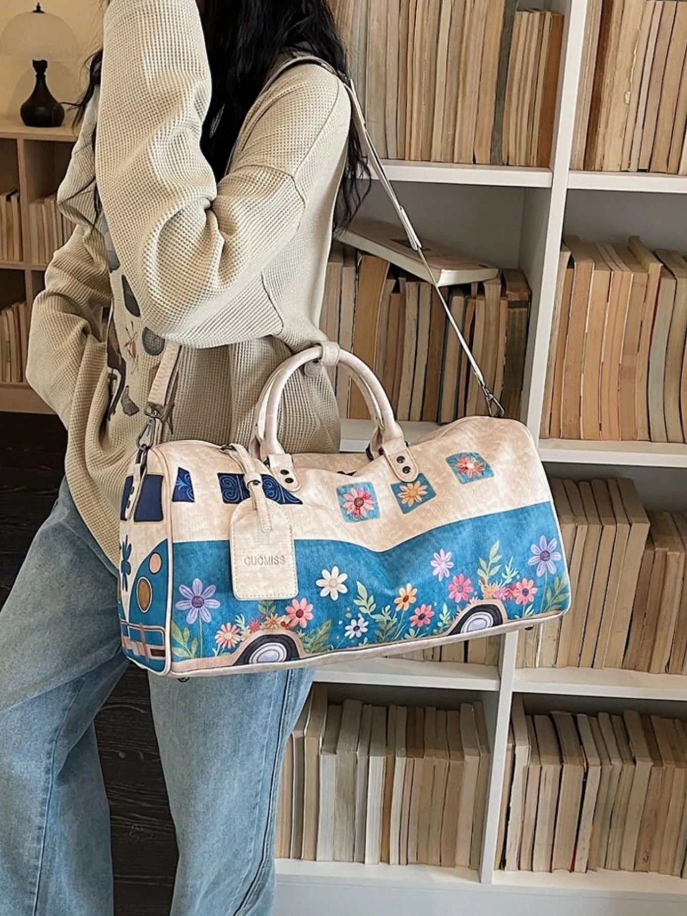 Person holding a floral-patterned handbag in front of a bookshelf