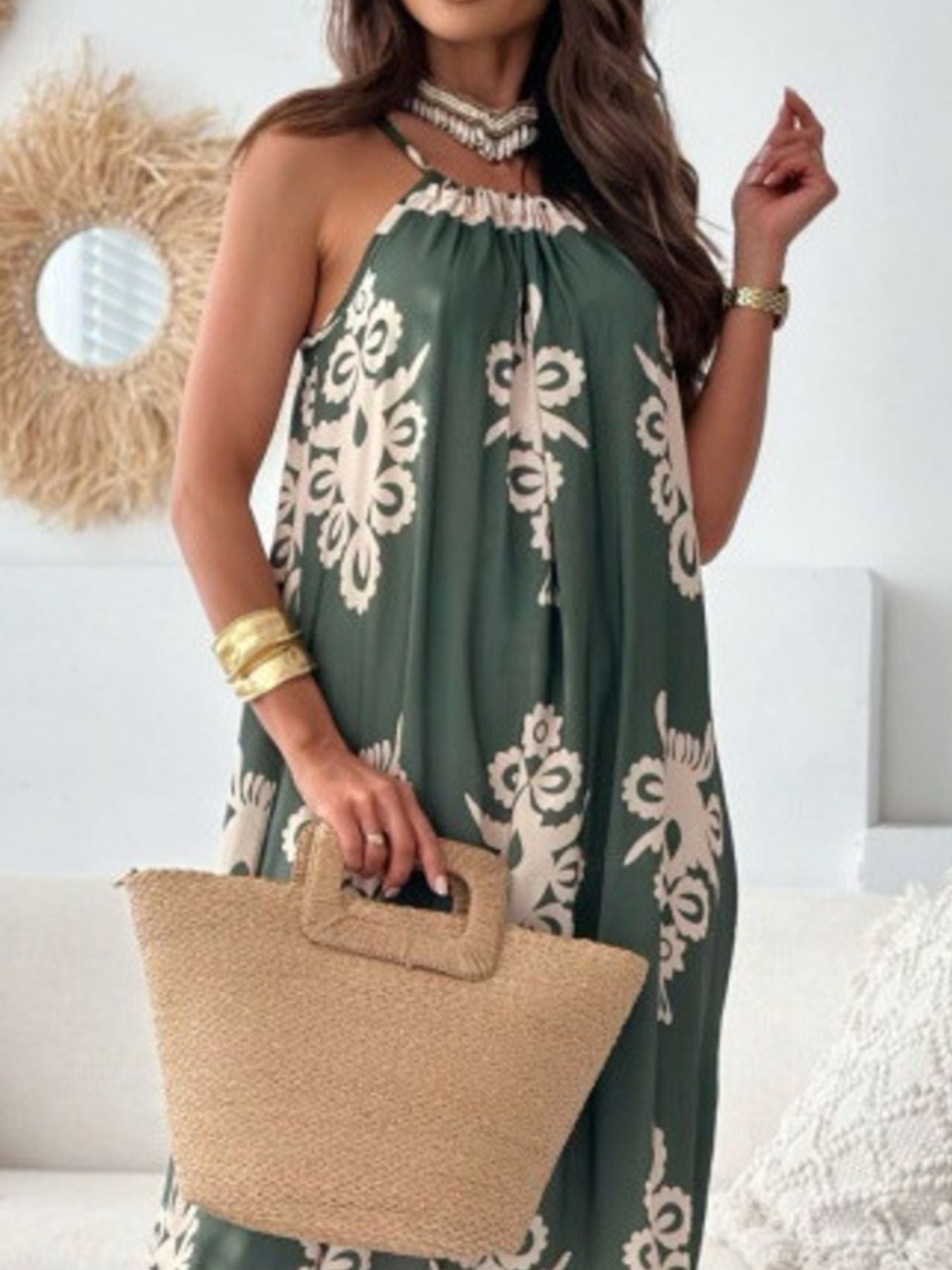 Woman wearing a green floral dress holding a straw bag indoors.