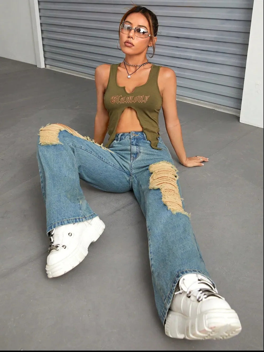 Person wearing a green tank top and ripped blue jeans sitting on a gray floor.