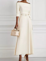 Woman wearing a white dress holding a beige handbag against a white background