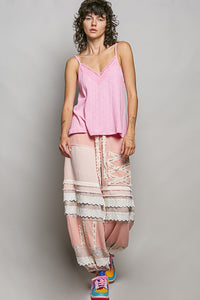 Woman wearing a pink top and layered pants with lace details against a plain background