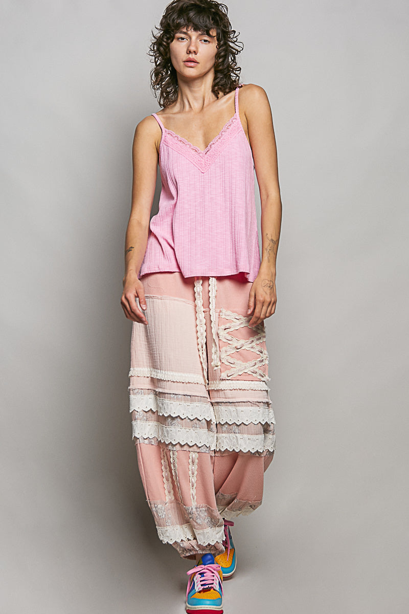 Woman wearing a pink top and layered pants with lace details against a plain background
