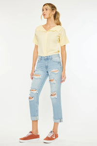 Woman wearing a yellow blouse and light blue ripped jeans on a white background
