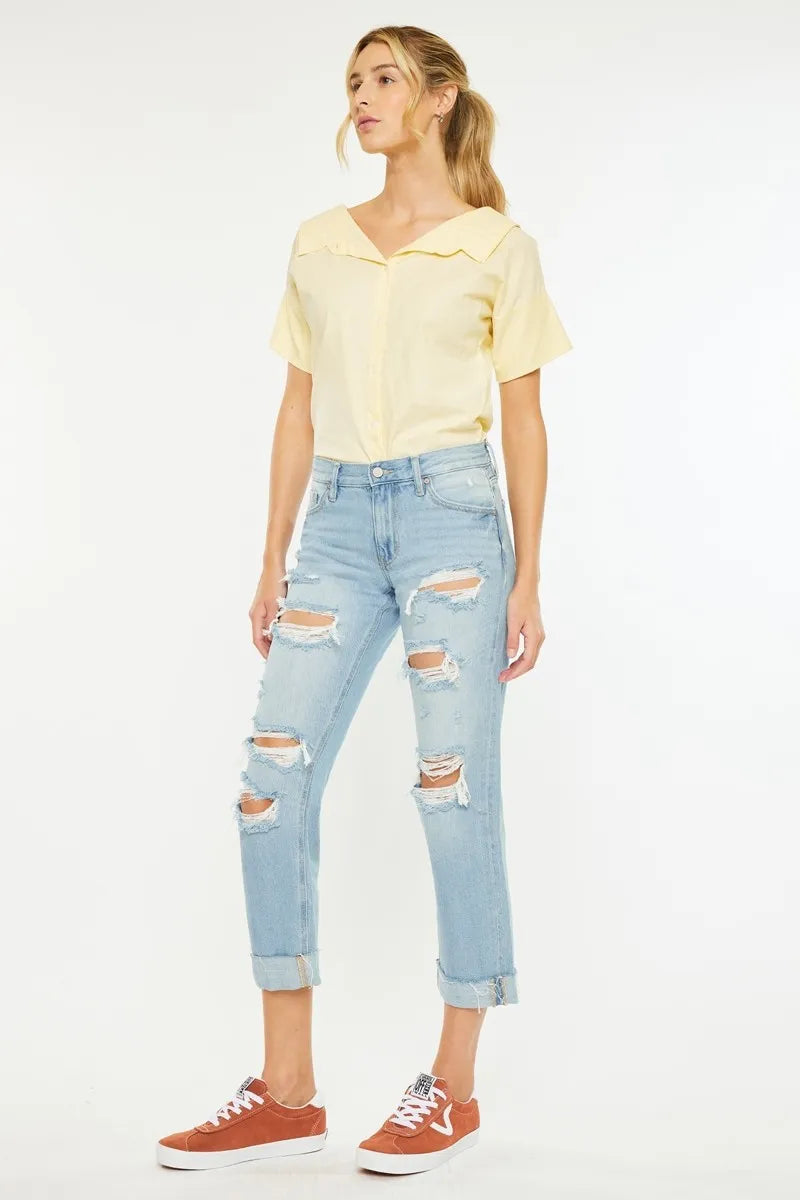 Woman wearing a yellow blouse and light blue ripped jeans on a white background