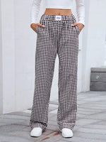Person wearing black and white checkered pants with a white top and shoes on a neutral background