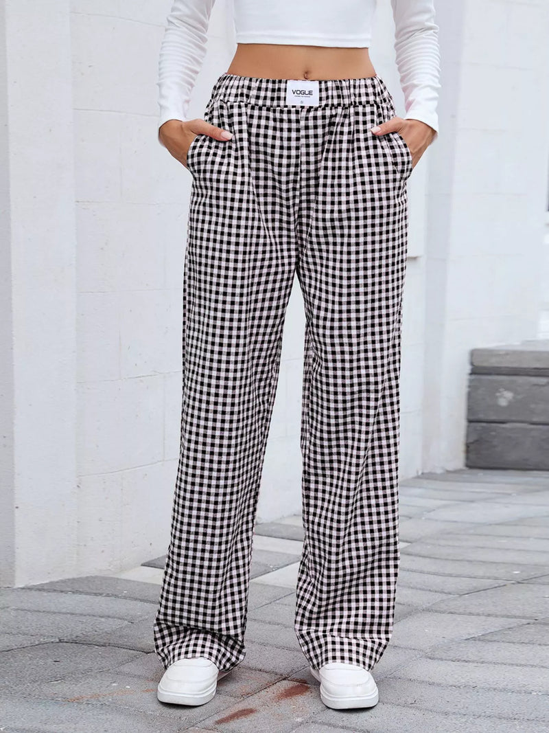 Person wearing black and white checkered pants with a white top and shoes on a neutral background