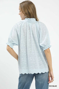 Woman wearing a light blue blouse with scalloped edges on a white background