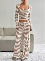 Woman wearing a striped long-sleeve top and wide-leg pants in a minimalistic setting.