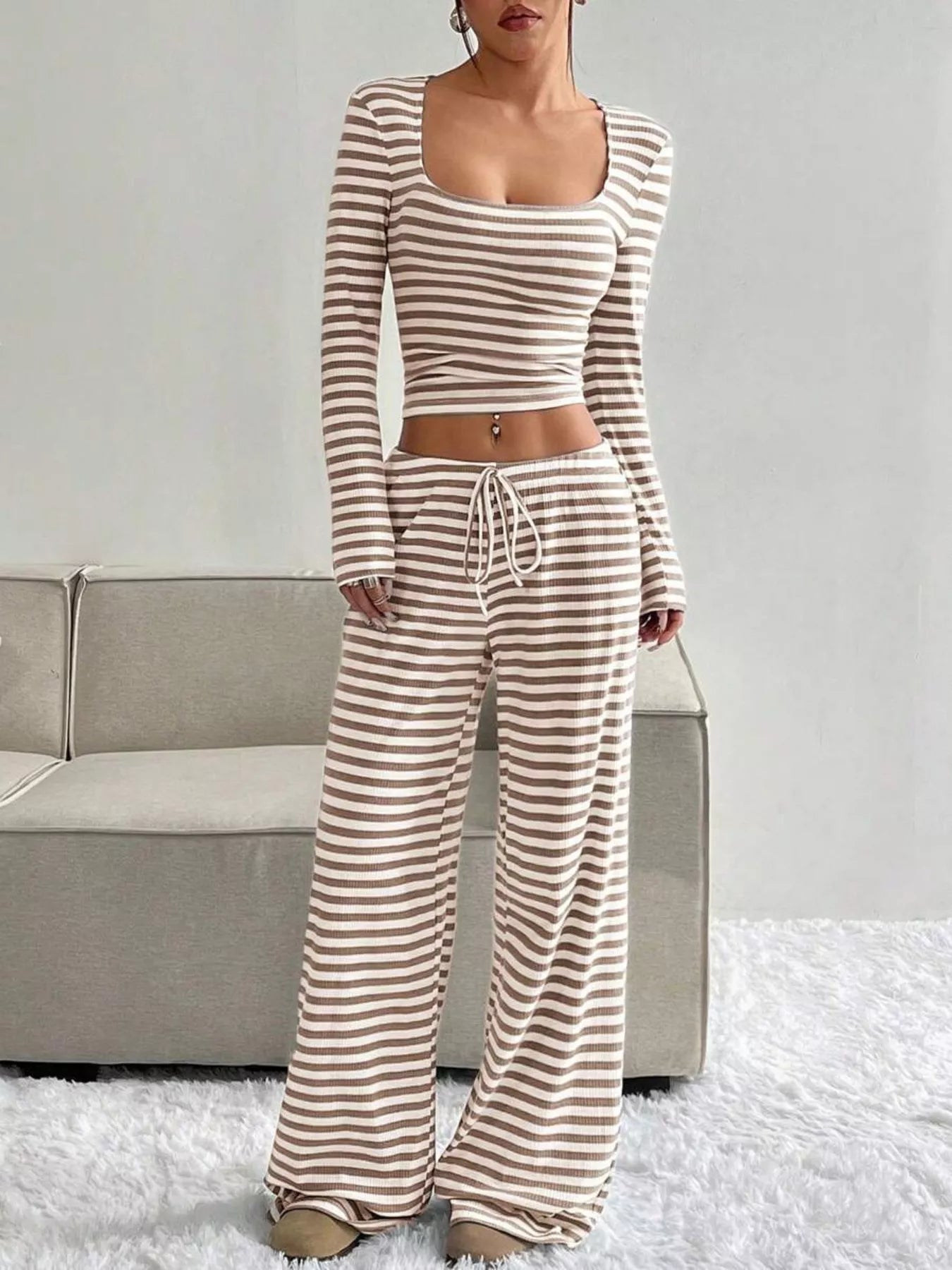 Woman wearing a striped long-sleeve top and wide-leg pants in a minimalistic setting.