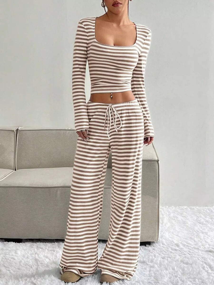 Woman wearing a striped long-sleeve top and wide-leg pants in a minimalistic setting.