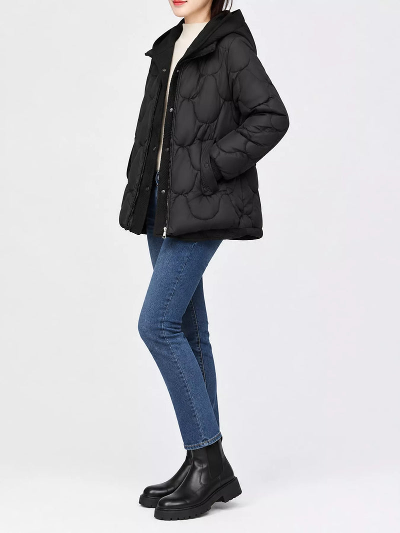 A model wearing a black quilted puffer jacket with a unique wavy, padded texture, paired with blue skinny jeans and black leather ankle boots, shot against a plain white studio background.
