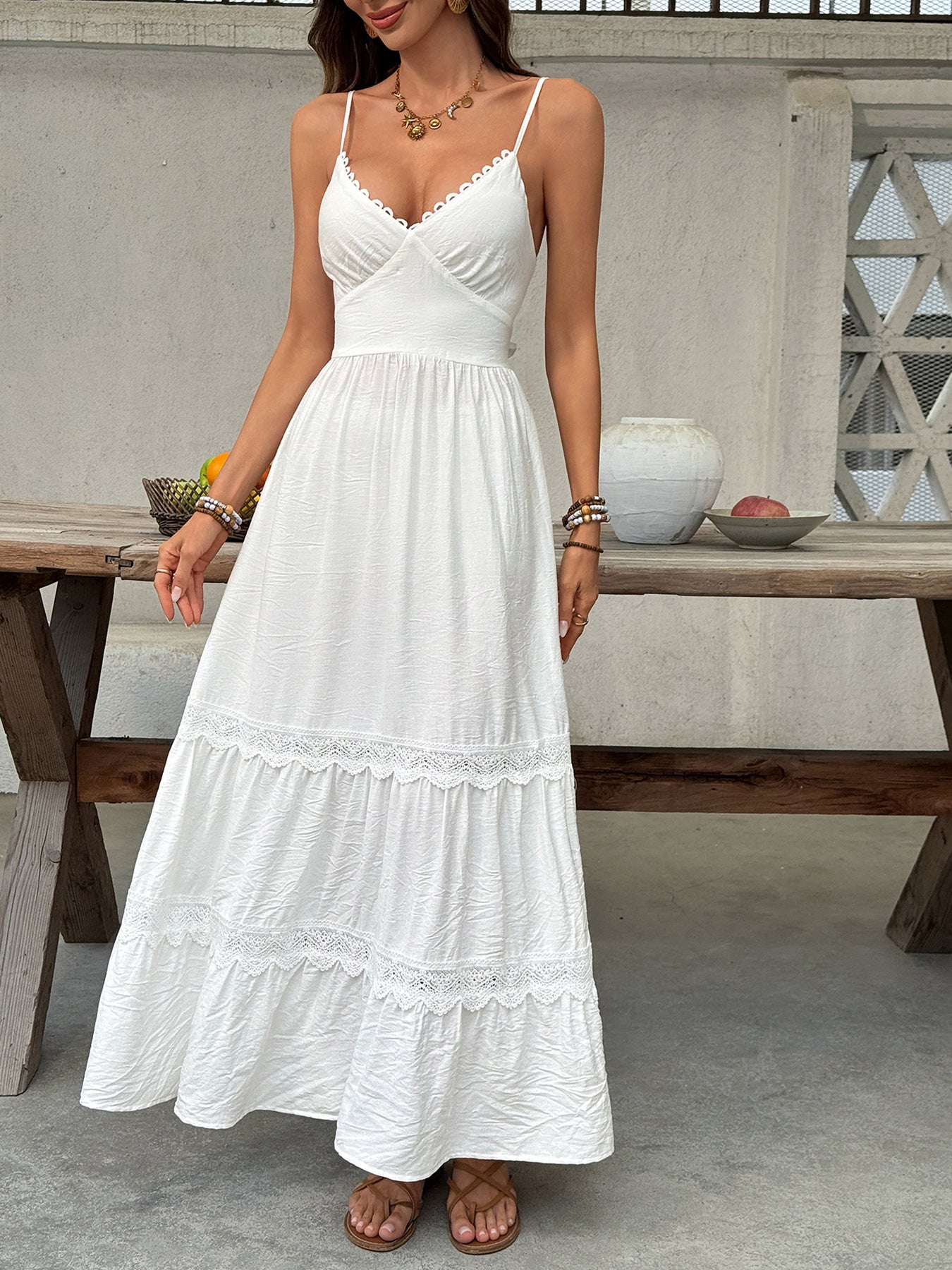 Woman wearing a white dress standing in front of a wooden table with decorative items.