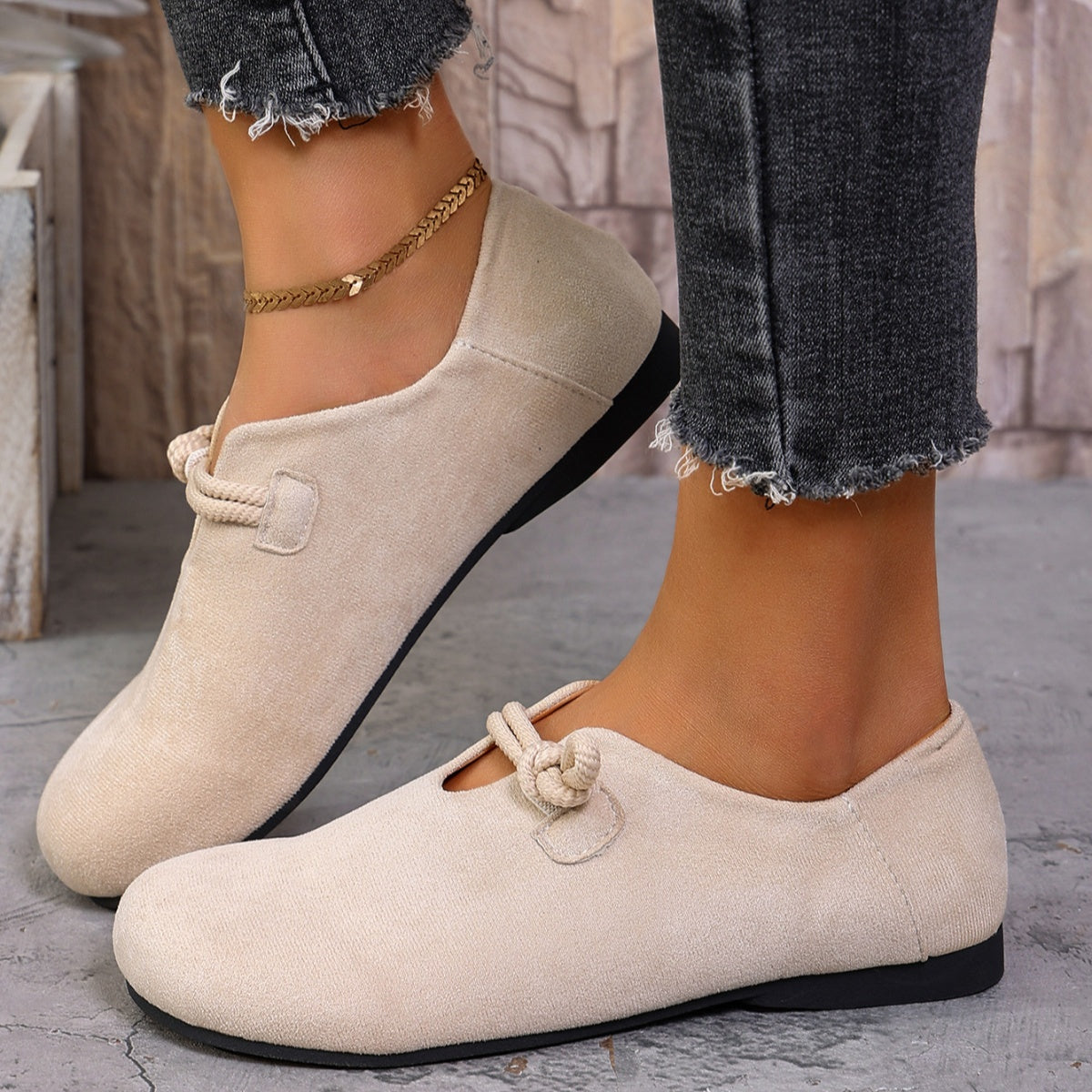 Beige loafers worn with jeans on a stone floor.