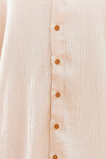 Close-up of a beige button-up shirt with visible buttons on a light background