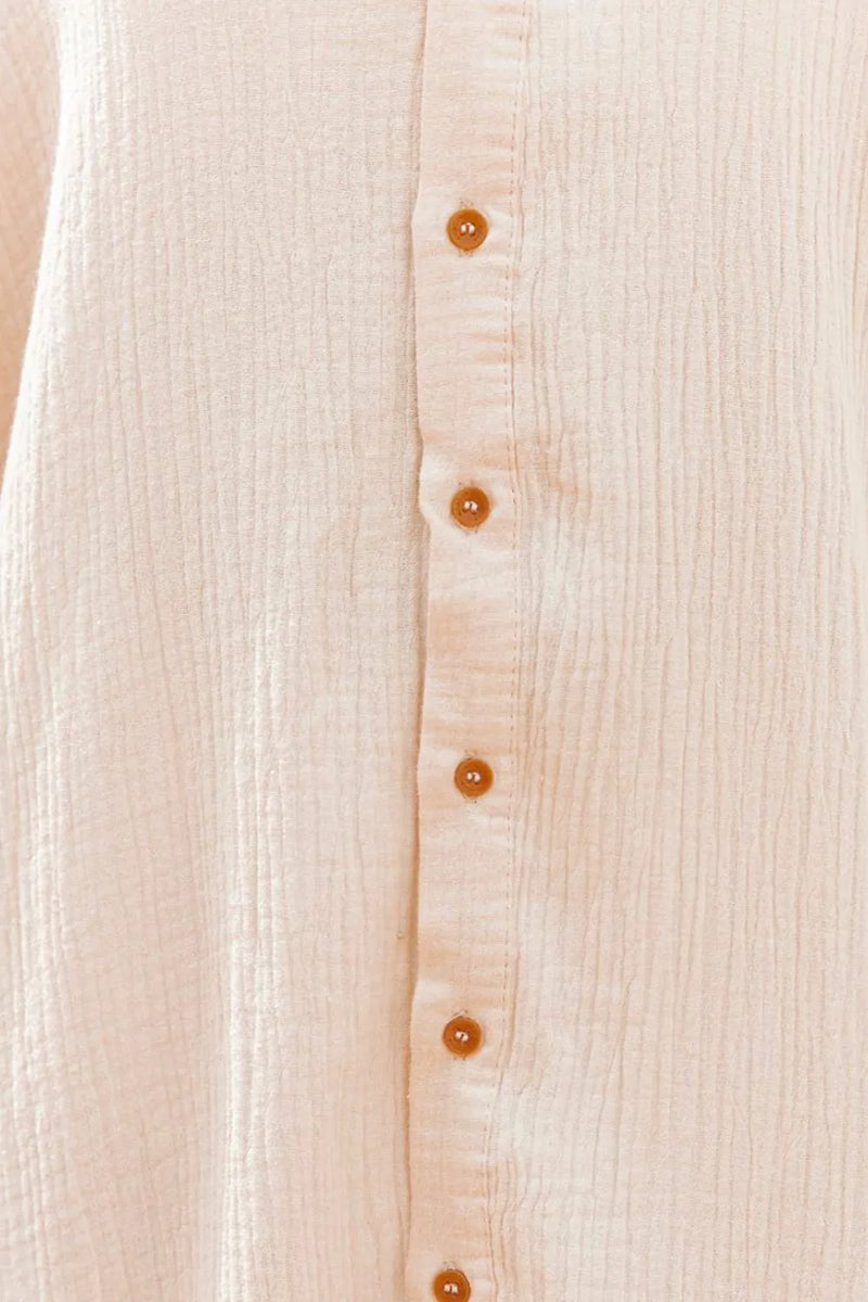 Close-up of a beige button-up shirt with visible buttons on a light background