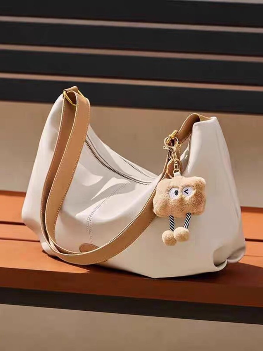 White handbag with a plush toy keychain on a wooden surface