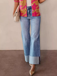 Person wearing a colorful jacket, blue jeans, and gold shoes on a plain background
