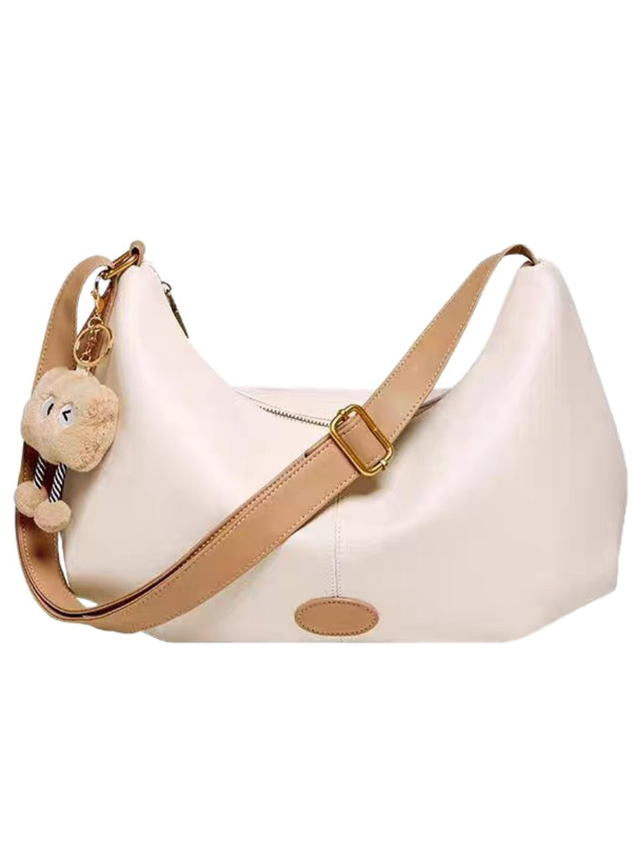 Beige handbag with a teddy bear charm on a white background