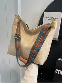 Beige handbag with a patterned strap on a mannequin against a white wall.