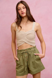 Woman wearing a beige knitted tank top and green shorts against a pink background
