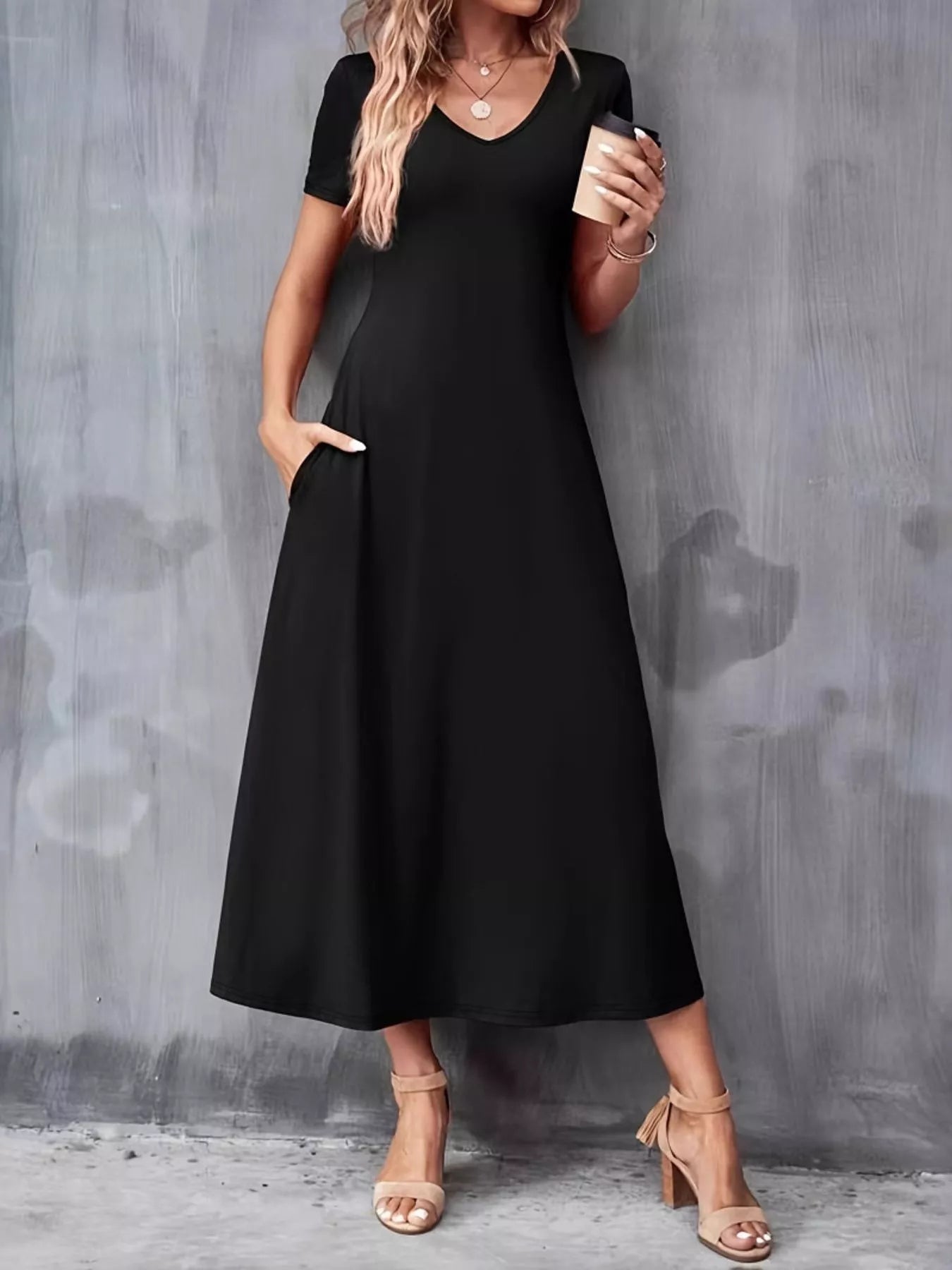 Woman wearing a black dress holding a coffee cup against a gray wall.